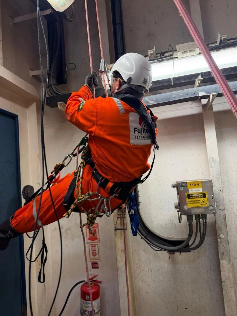 Fujitec technician on rope access working next to cable trays and electrical boxes